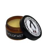 Open jar of 'Holdfast' balm with 'Penguin Tattoo Co.' lid on a white background